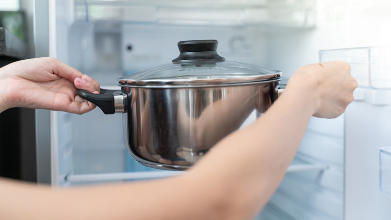 woman's arms putting silver pot on refrigerator shelf