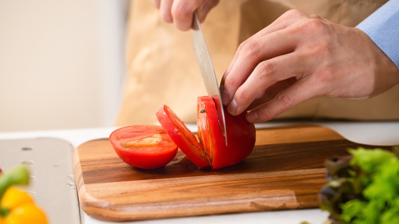 Person cutting tomato on board