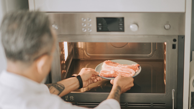 Man placing frozen meat in the microwave