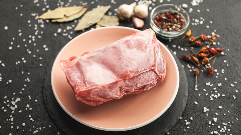 Frozen raw meat on plate surrounded by seasonings