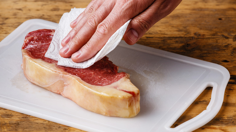 Hand dabbing steak with paper towel to remove excess moisture