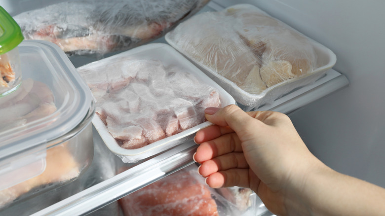 Hand taking frozen chicken out of freezer