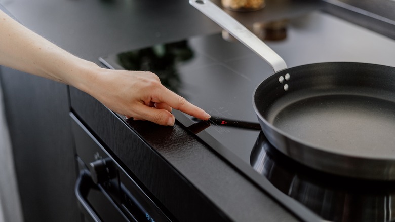 woman adjusting heat on stove by frying pan