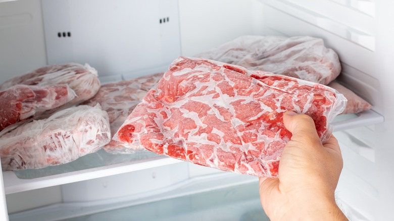 person putting package of raw meat into freezer