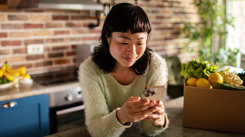 Woman in kitchen reading on her phone