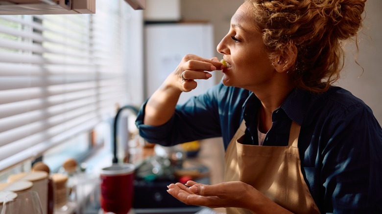 Woman taking a bite of food while she cooks