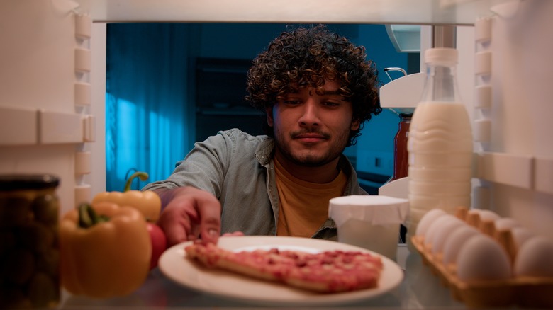 man getting pizza from fridge