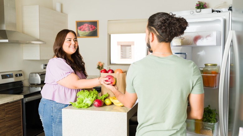 couple putting groceries in fridge