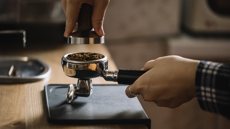 Barista tamping coffee grounds in group handle