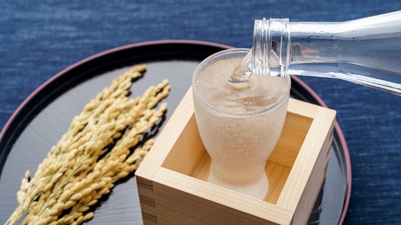 Sake being poured into a glass with rice stalks on a plate 