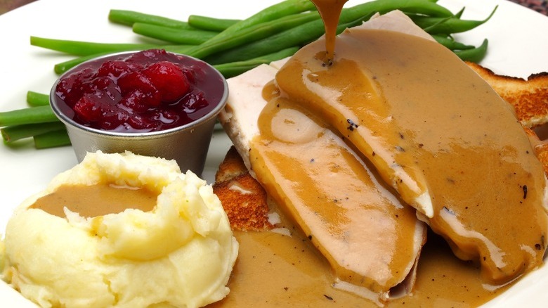 Sliced turkey covered in gravy next to mashed potatoes, green beans, and cranberry sauce