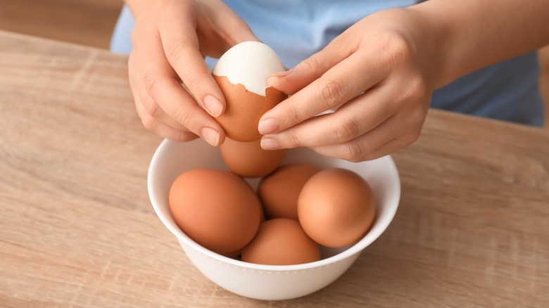Hands peeling a bowl of hard-boiled eggs