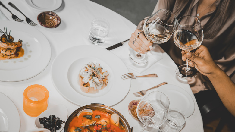 Diners eat in a fine dining setting with multiple pieces of silverware and plates on the table.