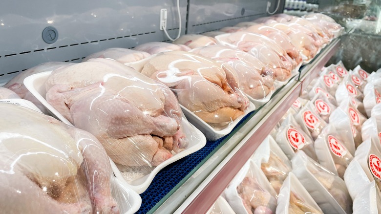 A selection of raw, whole chickens lines an aisle of a grocery store