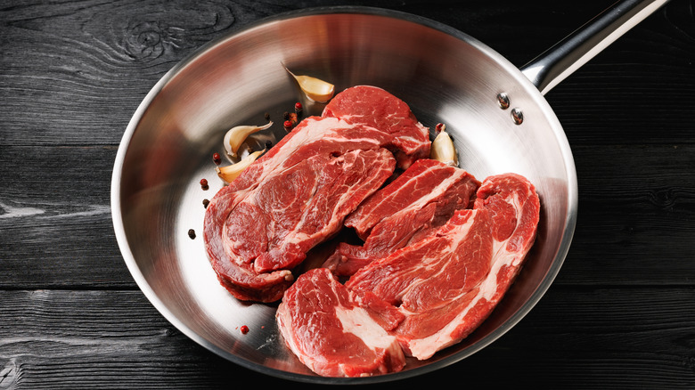 Two steaks sit in an aluminum pan next to aromatics