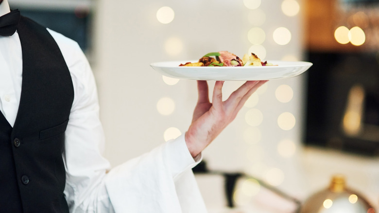 A fine dining waiter carries a plate of food to the table.