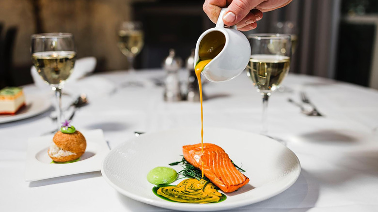 A waiter pours sauce over a salmon dish at the table.