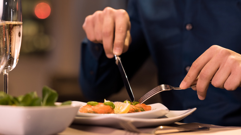 Someone eating a salad with a fork and knife at a restaurant