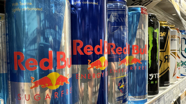 A line of energy drinks sit on a shelf in a grocery store