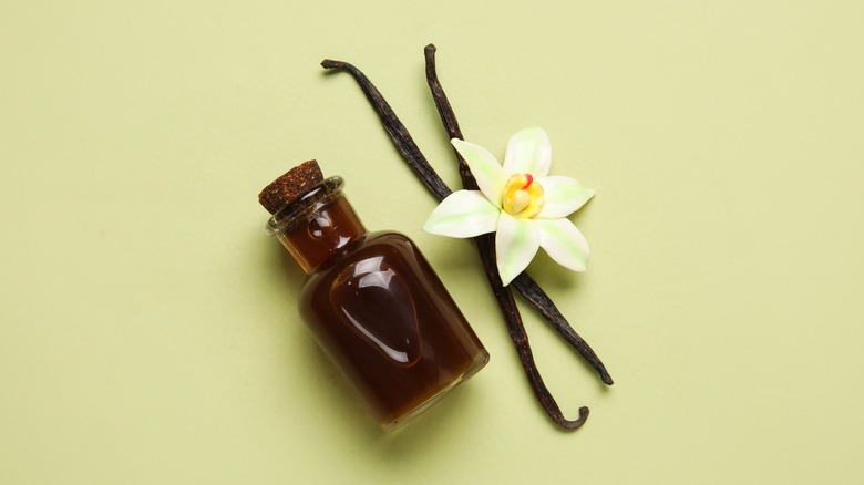 Vanilla extract in a bottle with vanilla beans and a flower.