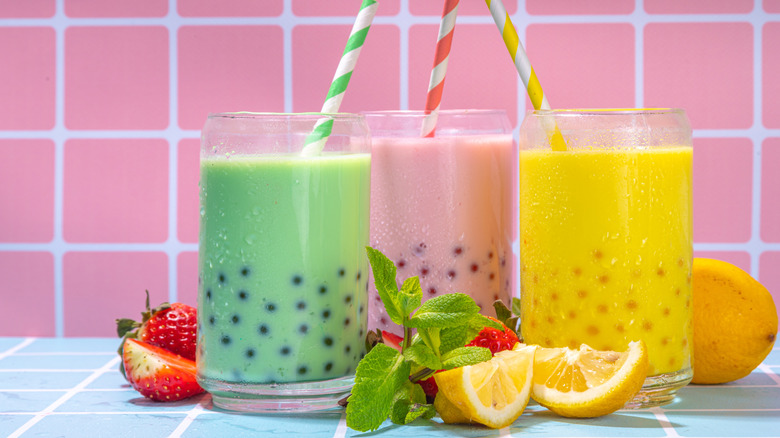 Set of three colorful summer bubble tea, bright creamy pearl tea or latte tapioca drinks, pink berry, yellow citrus, green mint, with tapioca balls and crushed ice, on colorful tile background