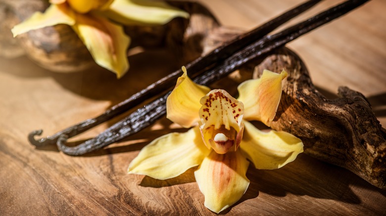 Vanilla flowers and pods on wooden surface