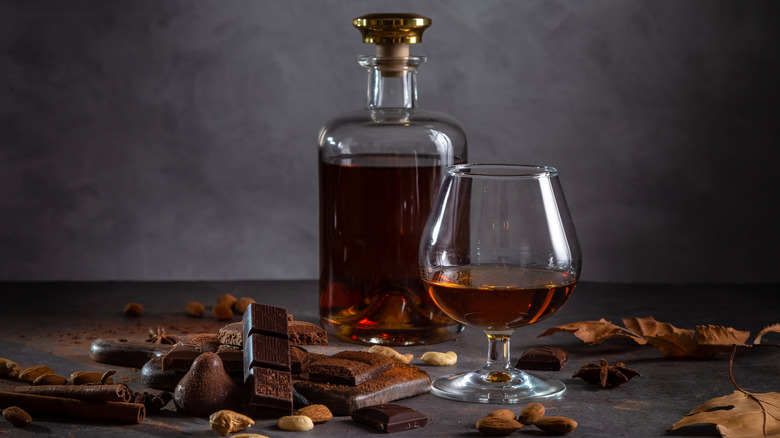 A bottle and glass of Cognac with chocolates and nuts