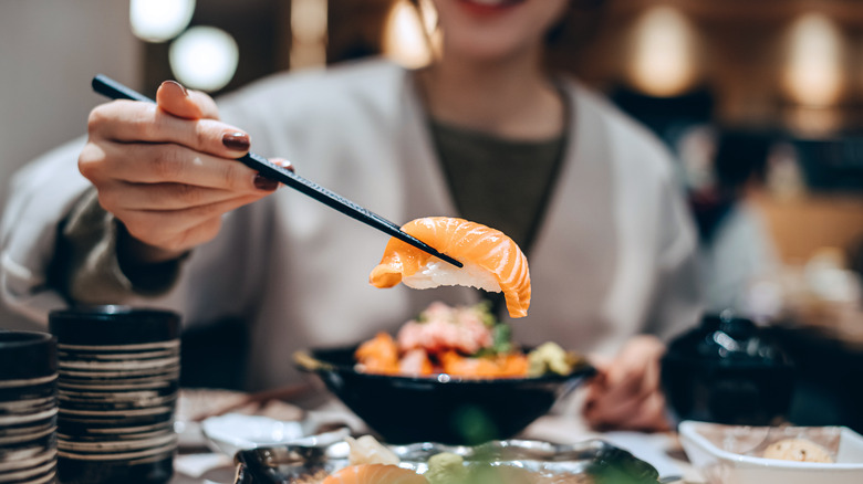 A person holding up a piece of salmon nigiri sushi using chopsticks.