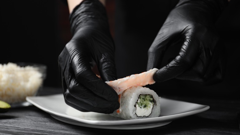 A sushi chef wearing gloves to prepare a maki roll.