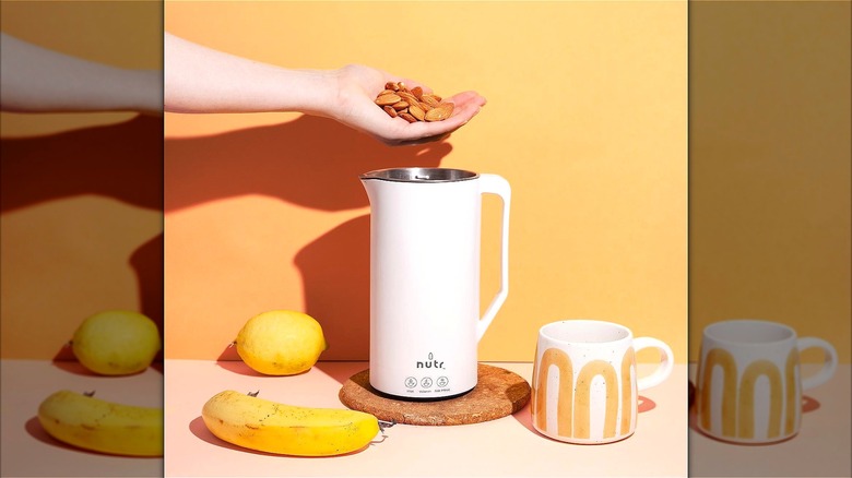 Hand holding raw almonds over a white Nutr nut milk machine