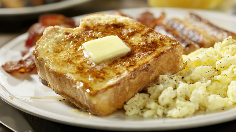 A slice of French toast is served with a side of eggs and bacon.