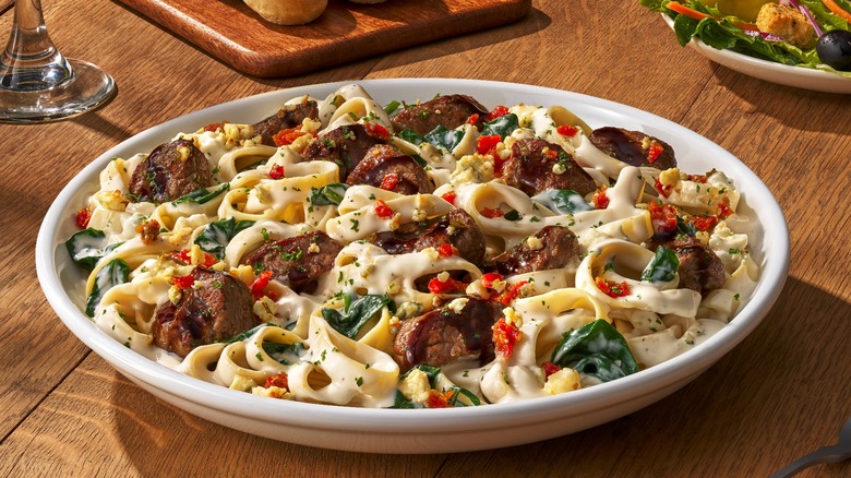 A white plate full of Olive Garden's Steak Gorgonzola Alfredo sits on a wooden table