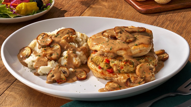 A white plate full of Olive Garden's Stuffed Chicken Marsala and a side of mashed potatoes sits on a wooden table