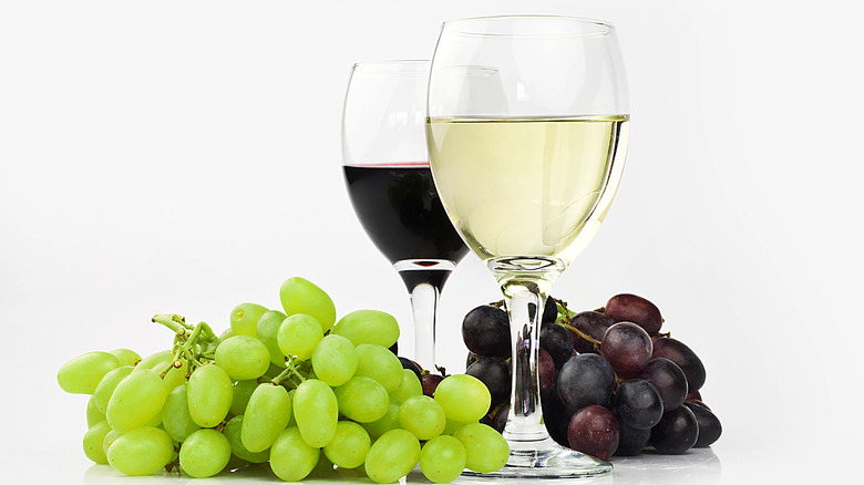 Glass of red and white wine next to green and red grapes