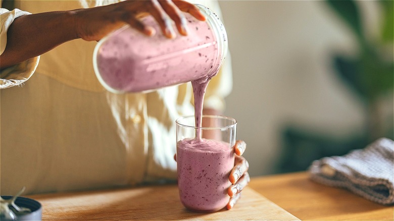 Hands pouring fruit smoothie from blender container into glass