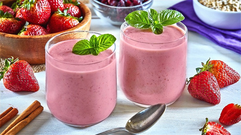 Two strawberry smoothies in glasses on a table garnished with mint