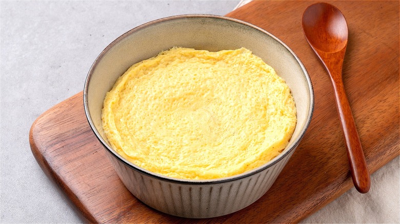 Steamed eggs in a white ramekin on a wooden board with a wooden spoon