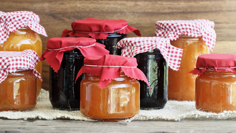 Various glass jars of homemade fruit jams with red cloths and red-and-white checkered cloths covering their tops