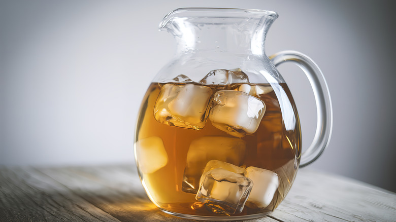 A pitcher full of large cubes of ice and cocktail sits on a wooden table