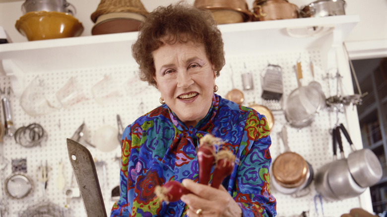 Julia Child smiling holding a knife and carrots