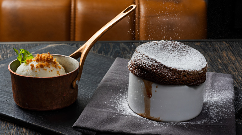 A soufflé being dusted in confectioner's sugar next to a pot of ice cream