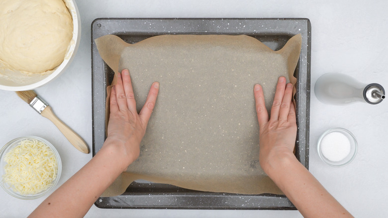 Hands lining baking pan with parchment paper