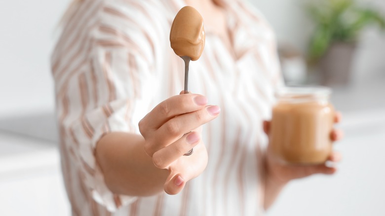 Person holding spoonful of peanut butter and jar