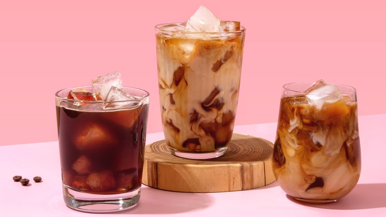 Three iced coffee drinks with cream on pink background