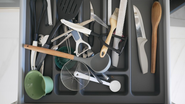 unorganized drawer containing silverware and kitchen tools