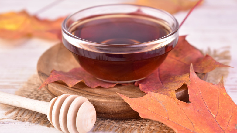 Maple syrup in a bowl surrounded by maple leaves