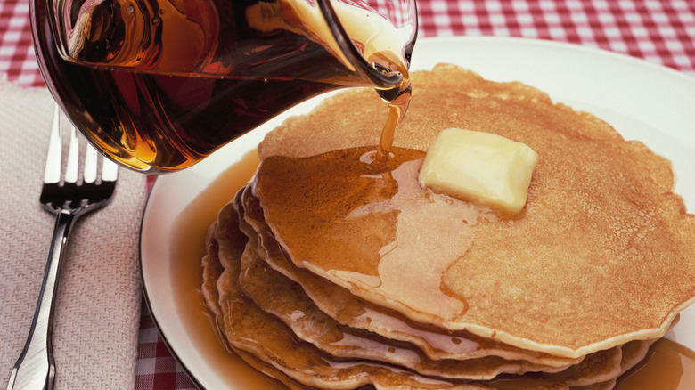 Pouring syrup onto a stack of pancakes topped with butter