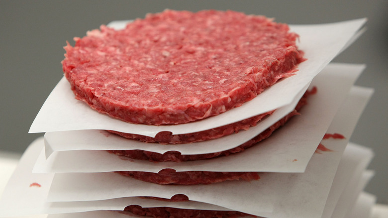 A stack of raw ground beef burger patties separated by white parchment paper