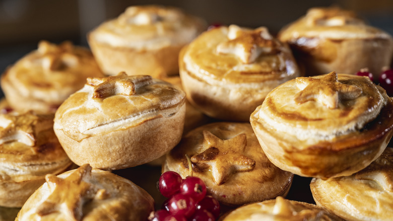 A close up shot of a stack of small baked mince pies with star details and holly berries