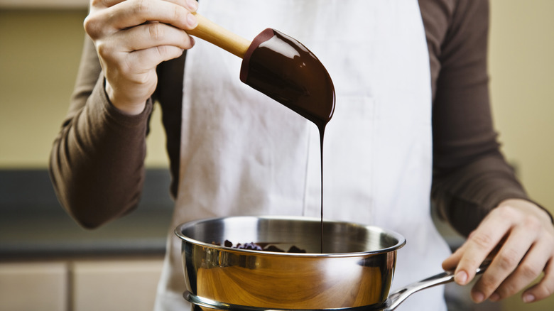 Person dripping melted chocolate off of a pastry spatula into a sauce pan